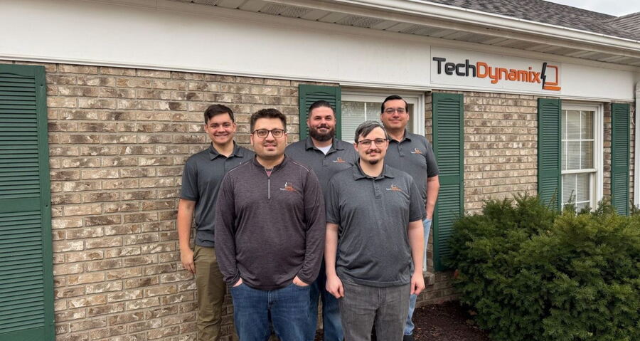 Five members of the Tech Dynamix team standing outside the company's office, below the Tech Dynamix sign.