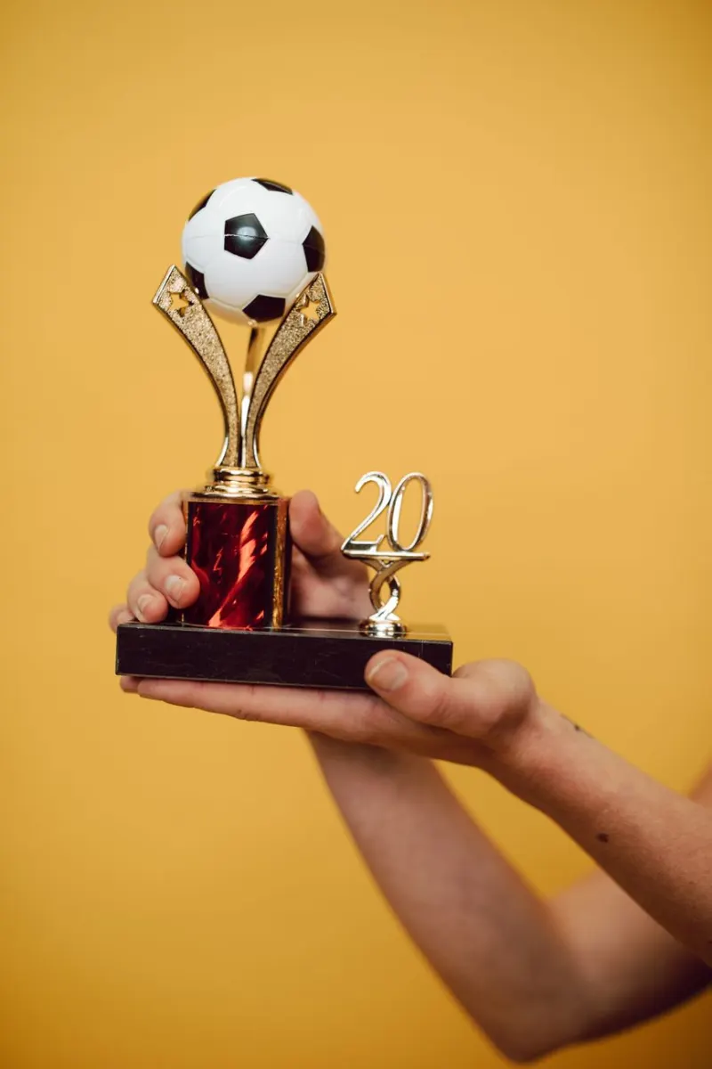 Close-up of hands holding a trophy against a bright yellow backdrop.